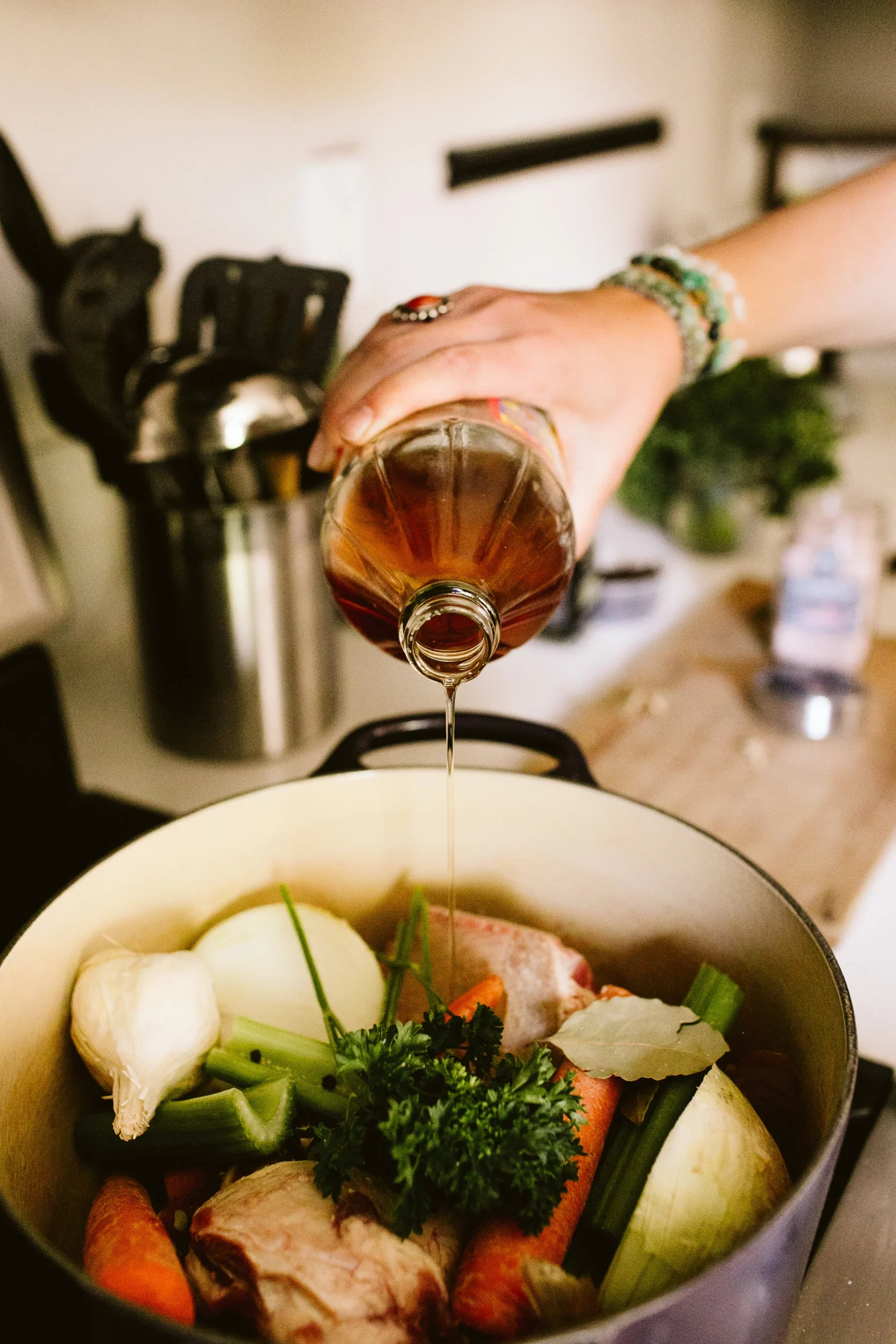 Vinegar being poured into a pot of chicken, carrots, onion, garlic, celery, and herbs for stock