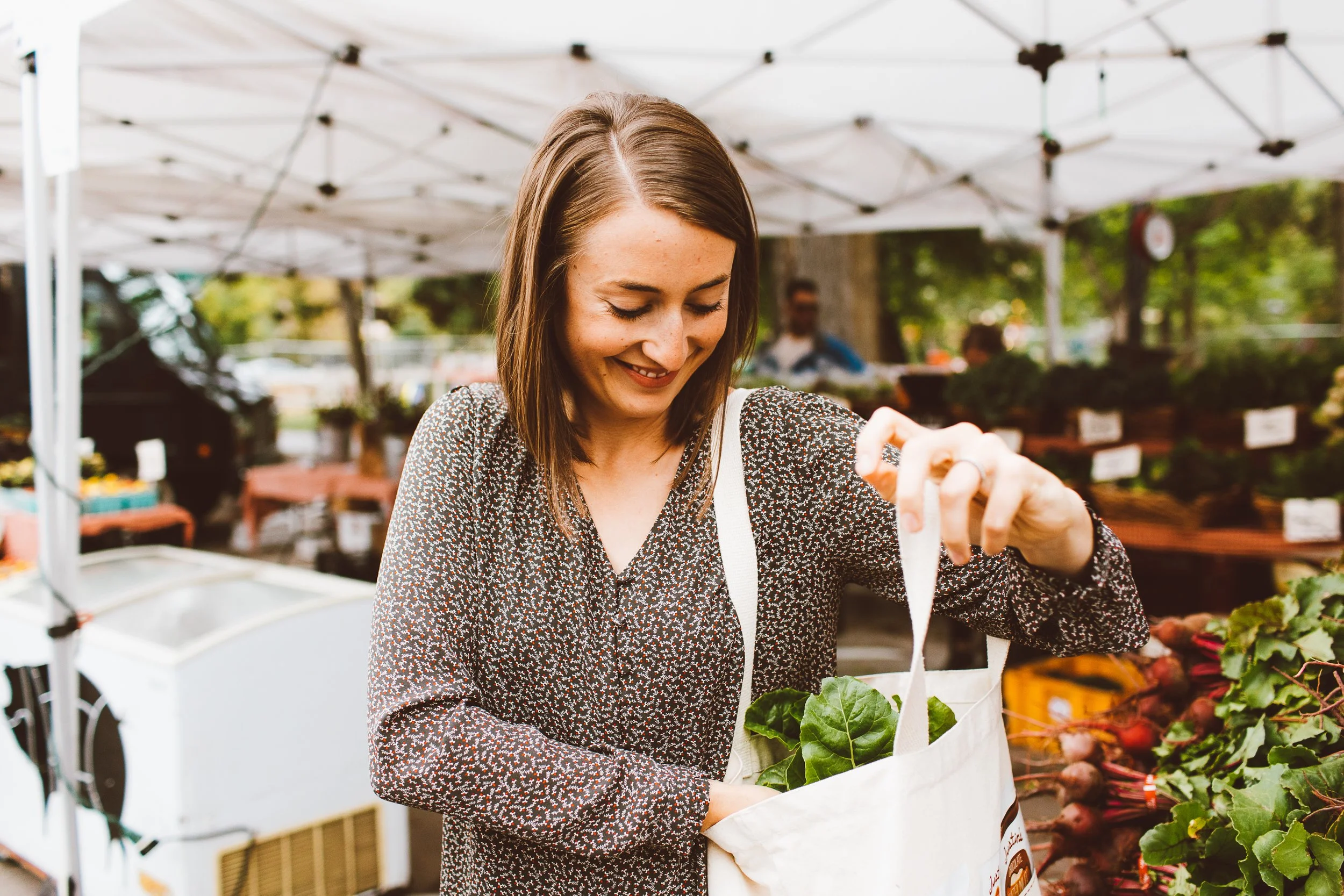 Woman smiling while placing leafy greens into a tote bag at an outdoor farmers market