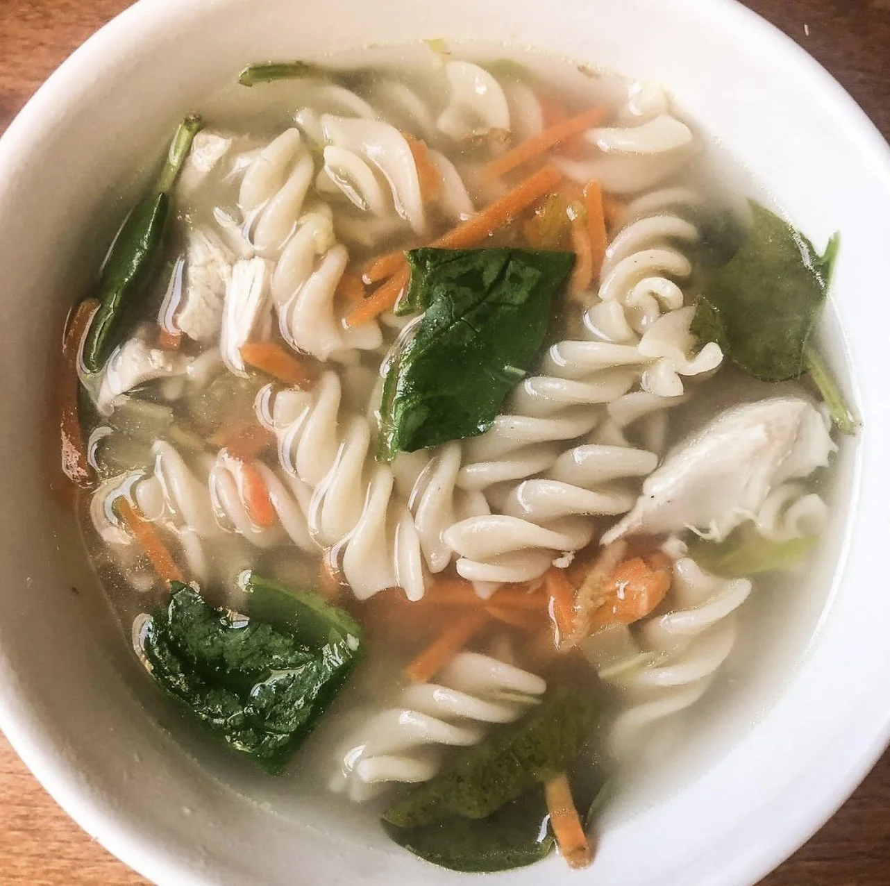 Bowl of chicken soup with fusilli pasta, carrots, and spinach leaves in broth
