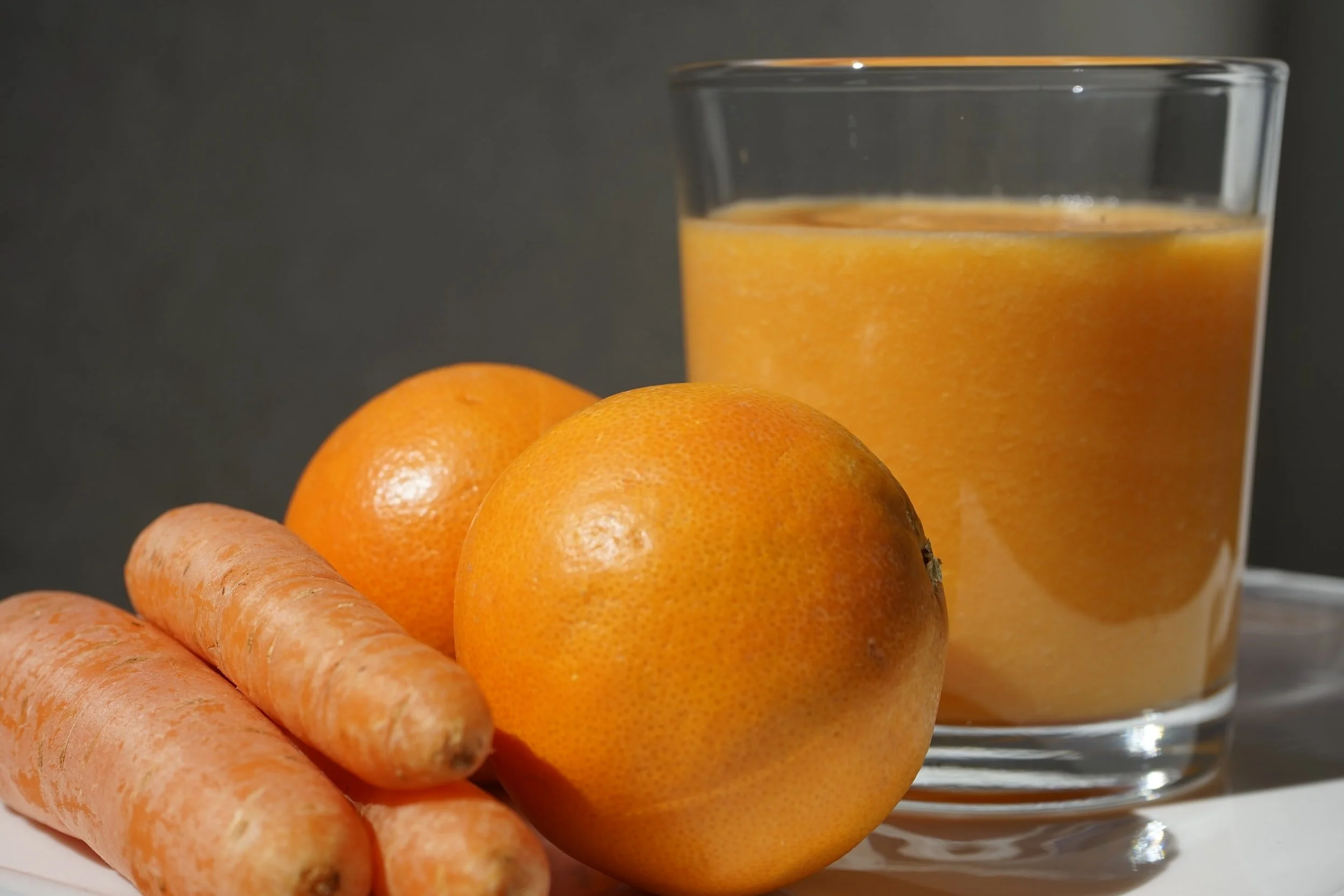 Glass of carrot-orange juice next to fresh carrots and oranges