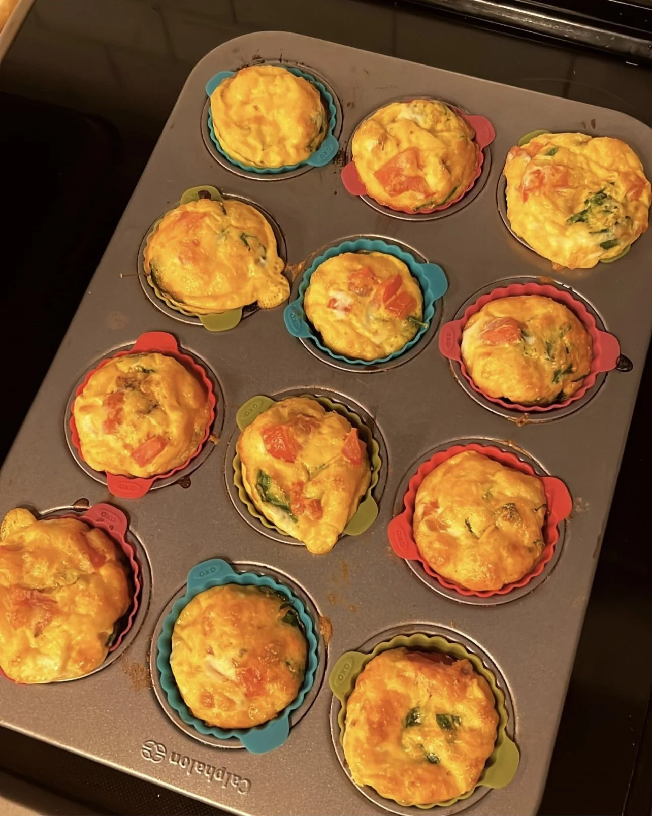 Baked egg muffins with tomato and spinach in a muffin tin with colorful silicone liners