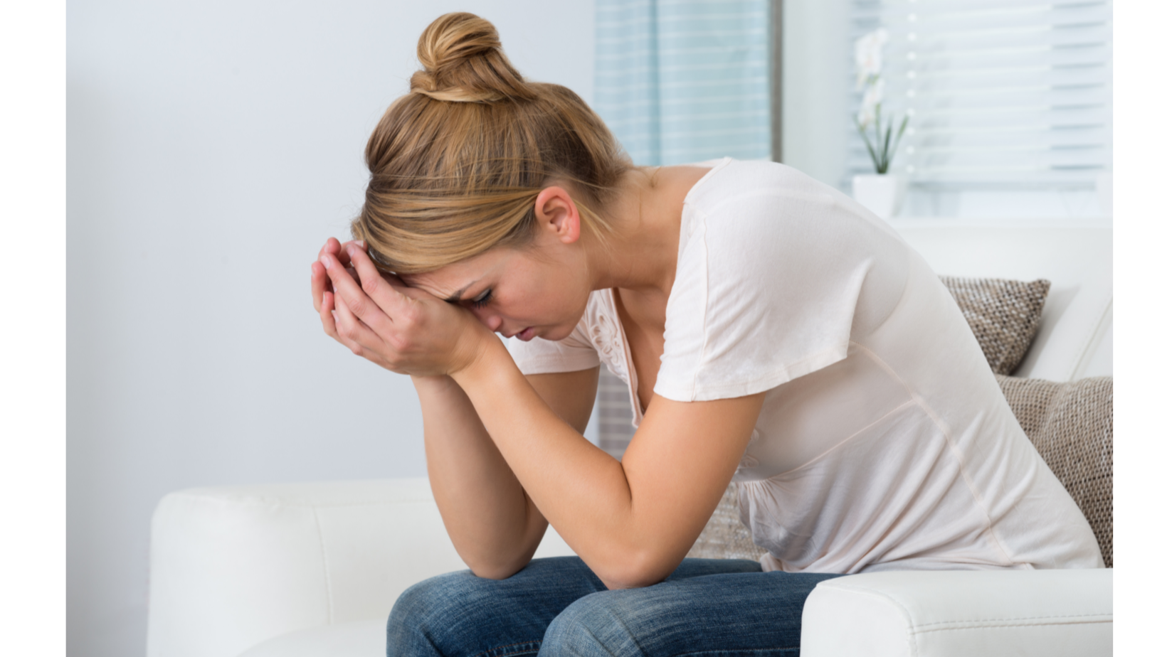 Woman sitting on a couch with head bowed into her hands, appearing distressed or upset