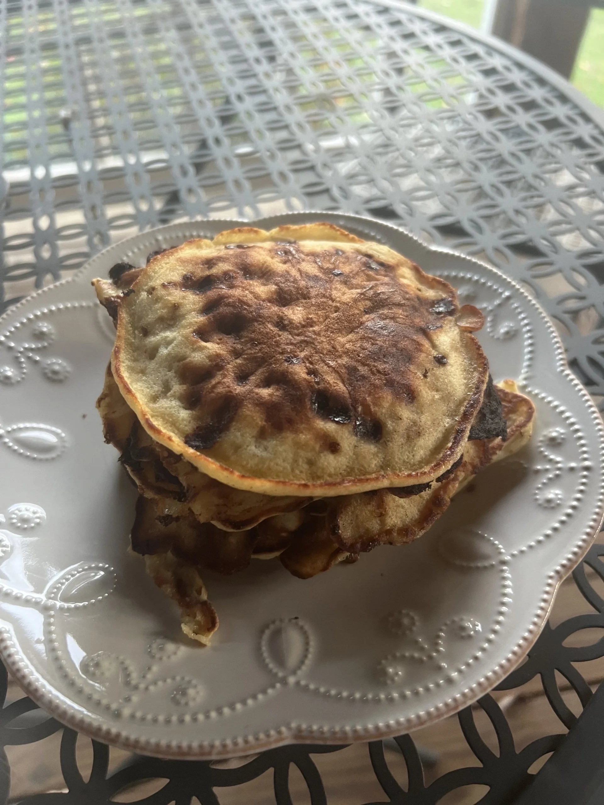 Stack of unevenly browned, charred pancakes on a decorative white plate
