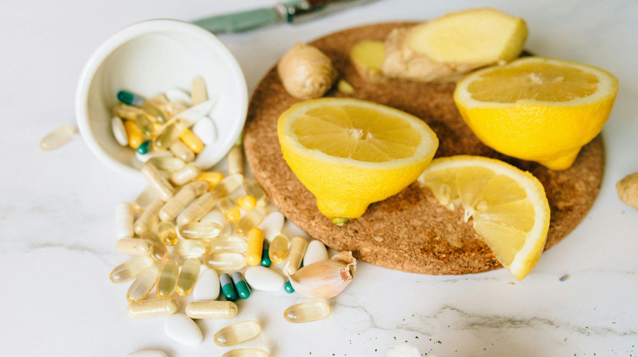 Assorted vitamin capsules and pills spilled beside sliced lemons, ginger, and garlic on a cutting board