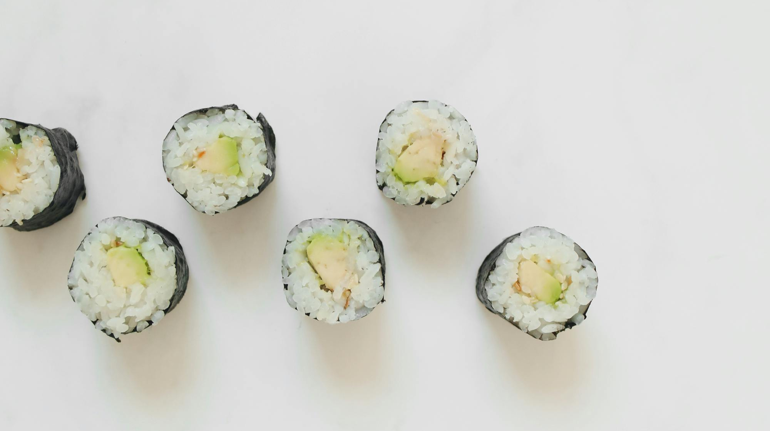Sushi rolls with avocado and fish filling, cut into pieces on a white surface