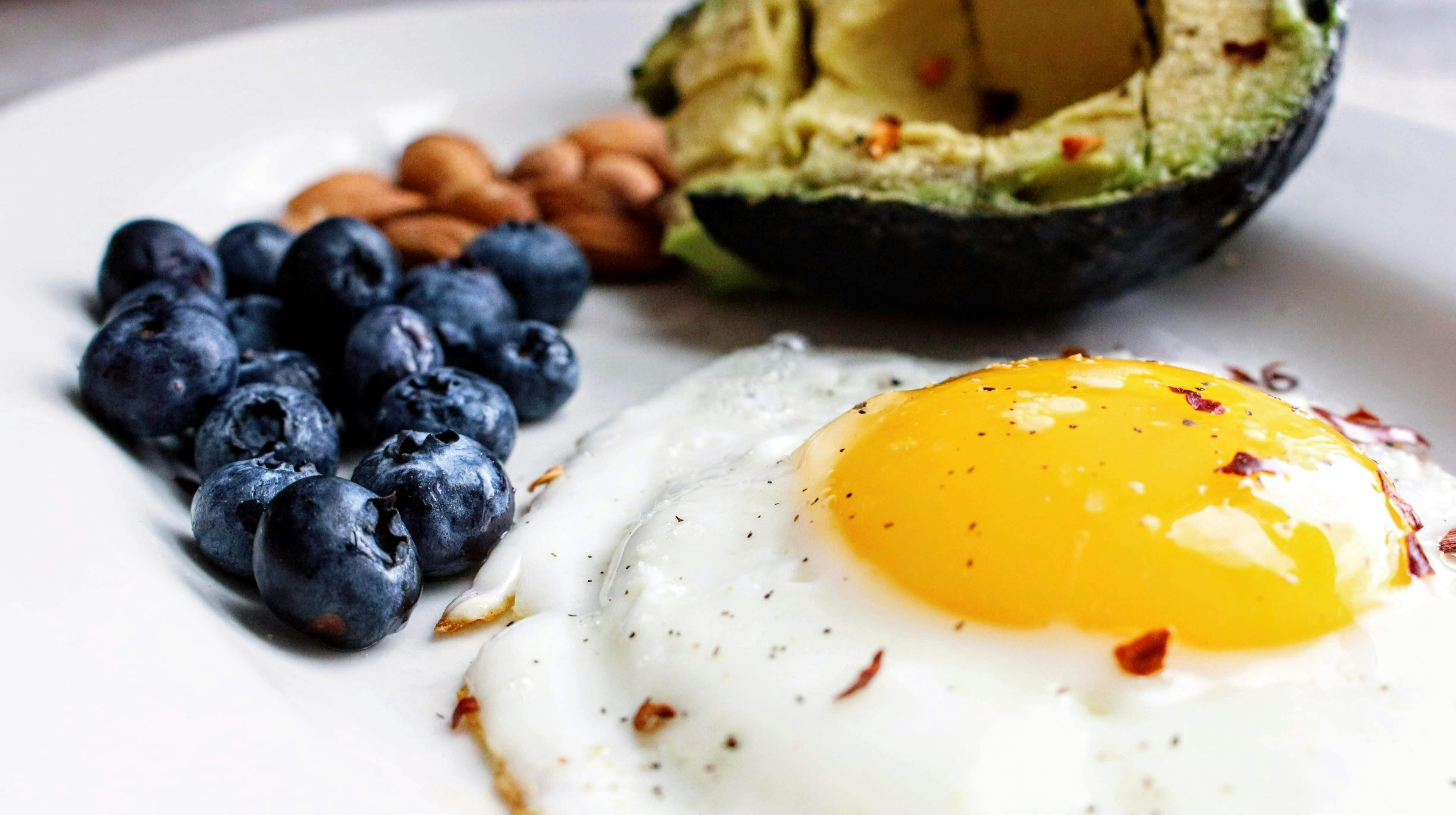 Plate with a fried egg topped with chili flakes, fresh blueberries, almonds, and half an avocado