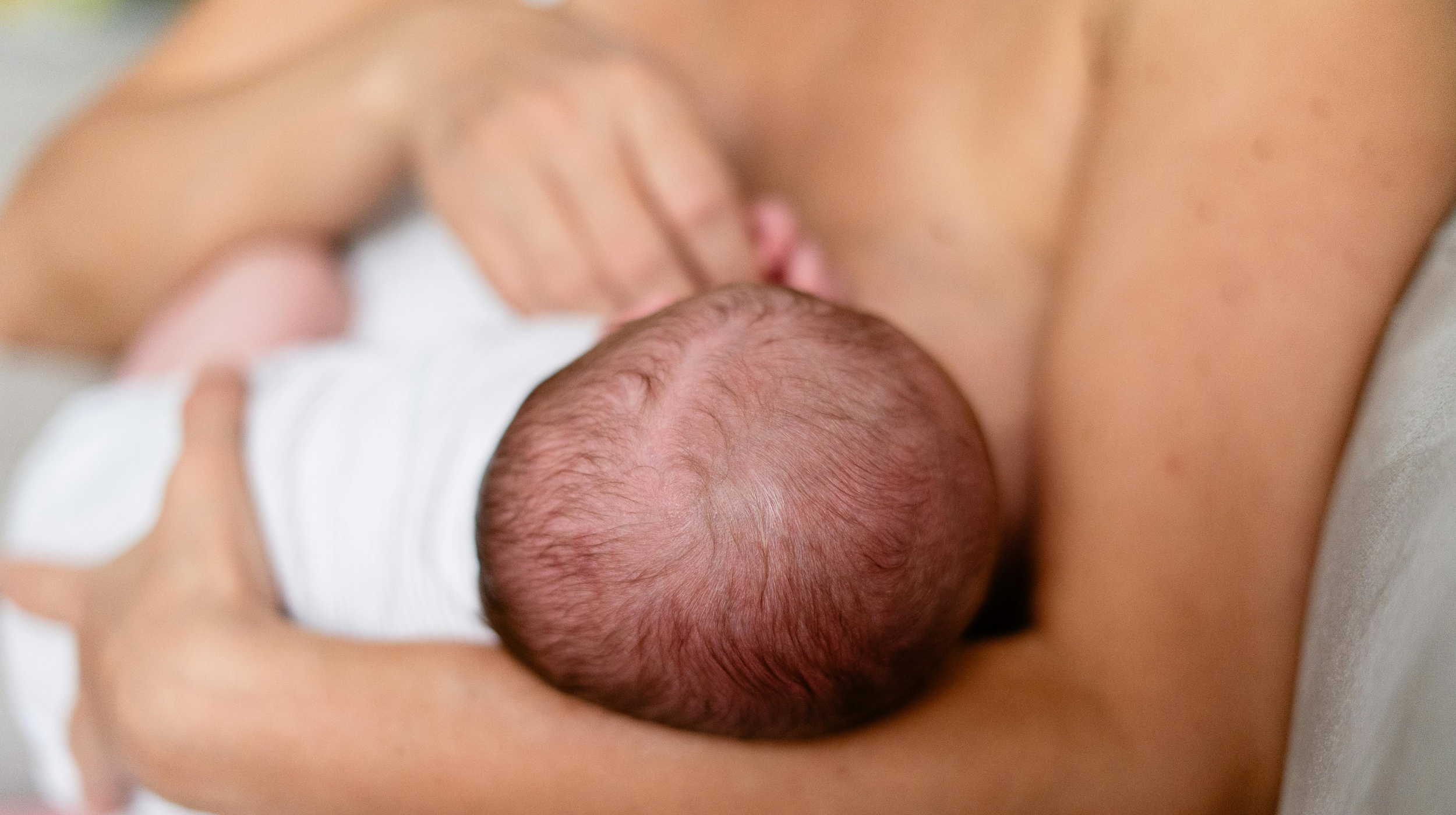 Close-up of a newborn baby's head being cradled against a parent's bare chest
