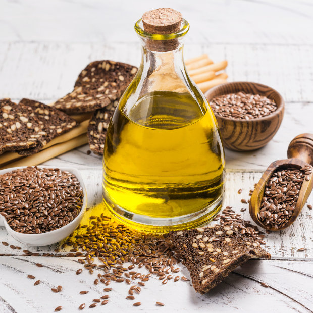 Bottle of flaxseed oil surrounded by flax seeds and crispbread crackers on a wooden table