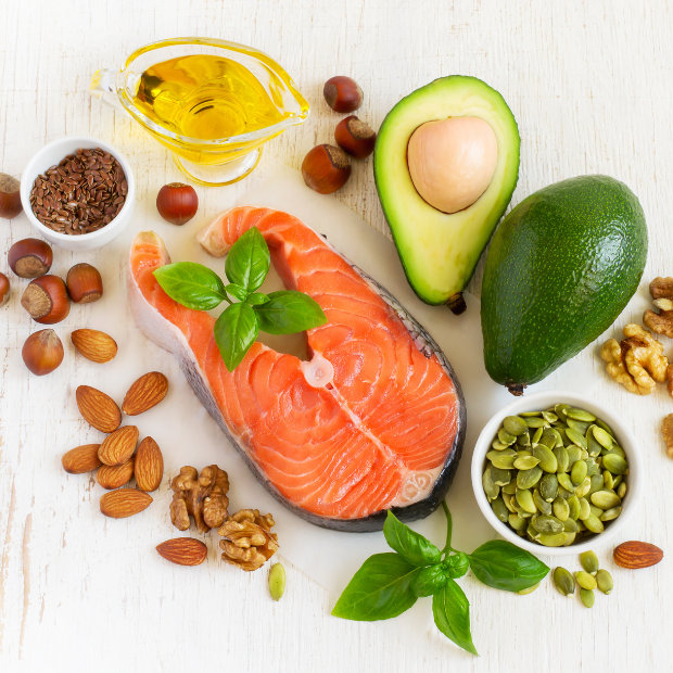 Salmon steak, avocado, walnuts, almonds, hazelnuts, flax seeds, pumpkin seeds, and oil arranged as sources of healthy fats