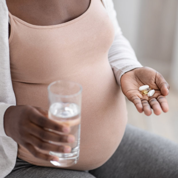 Pregnant woman holding a glass of water in one hand and vitamin pills in the other