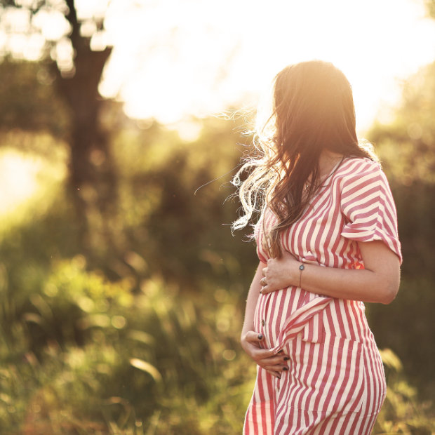 Pregnant woman in a striped dress cradling her belly, standing outdoors in golden sunlight