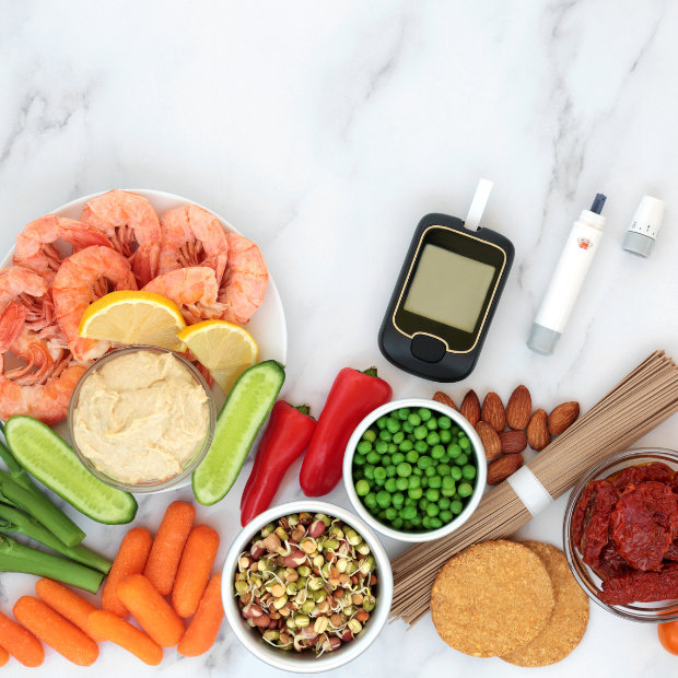 Plate of shrimp, hummus, vegetables, nuts, and whole grains beside a blood glucose meter and insulin pen