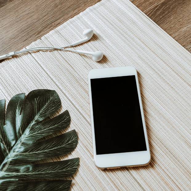 Smartphone with earbuds and a palm leaf on a woven mat