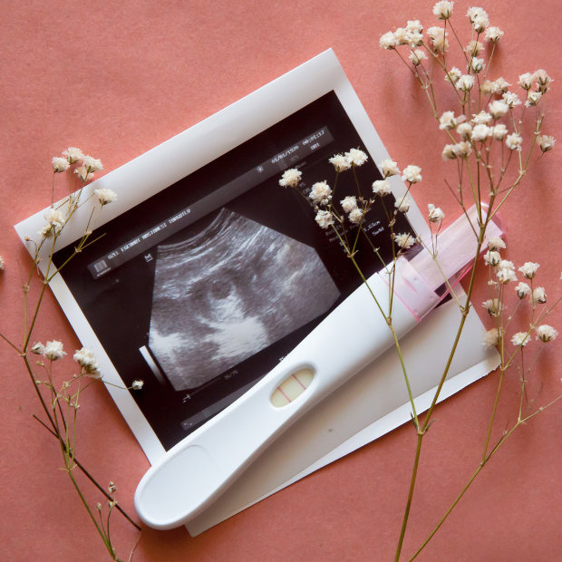 Ultrasound photo and pregnancy test lying on a pink background, surrounded by baby's breath flowers