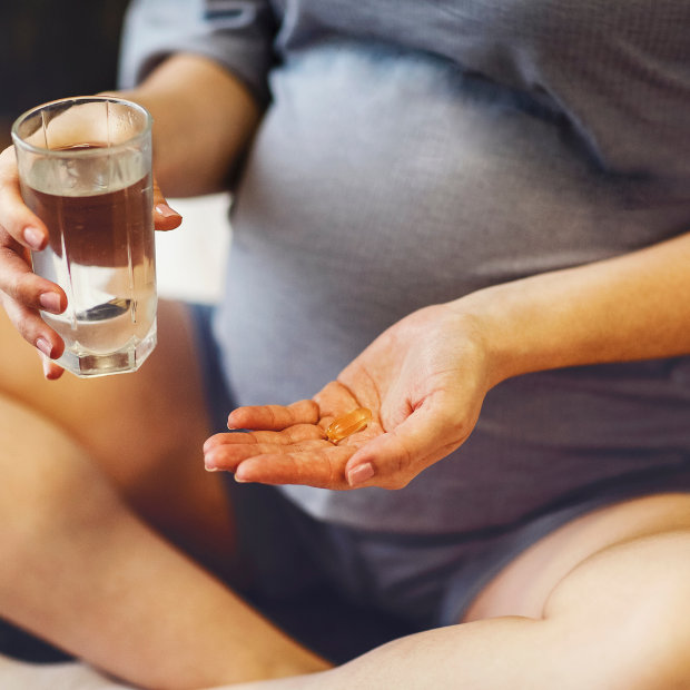 Pregnant woman holding a glass of water and a supplement capsule in her palm