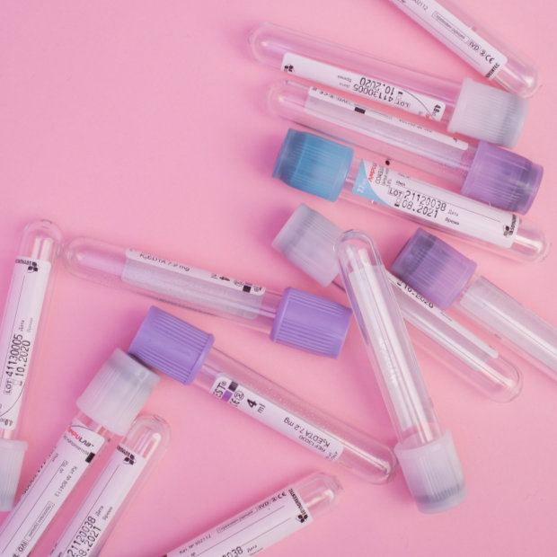 Several empty blood collection tubes with colored caps and lot number labels scattered on a pink background