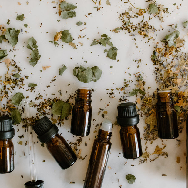 Amber essential oil bottles surrounded by scattered dried herbs and leaves on a white surface