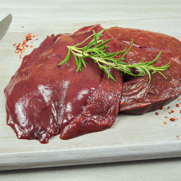 Raw liver garnished with rosemary sprigs and chili flakes on a wooden cutting board