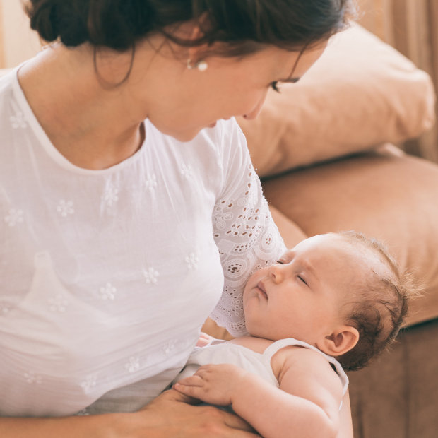 Mother in white lace top gazing at sleeping baby cradled in her arms
