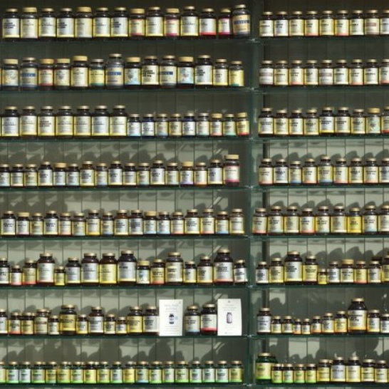 Shelves lined with rows of amber and clear supplement bottles with gold caps and colorful labels