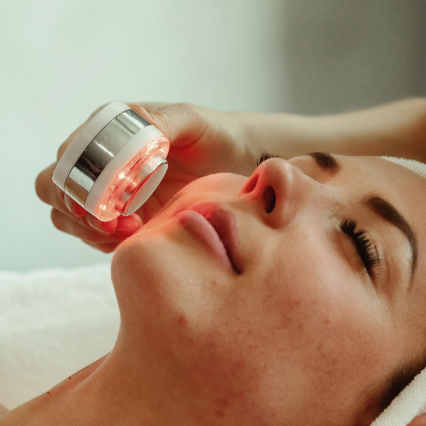 A red LED light therapy device applied to a woman's cheek during a facial treatment