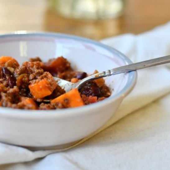 Bowl of chili with ground meat, kidney beans, and sweet potato chunks, fork resting inside