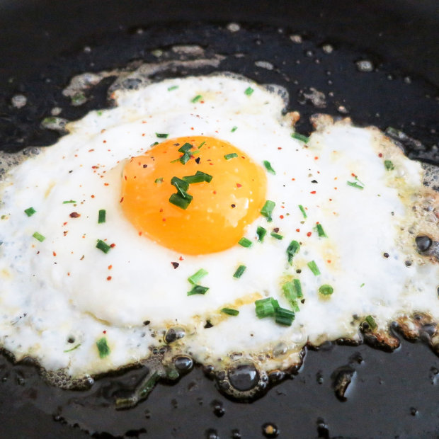 Fried egg in a pan, topped with chopped chives and red pepper flakes